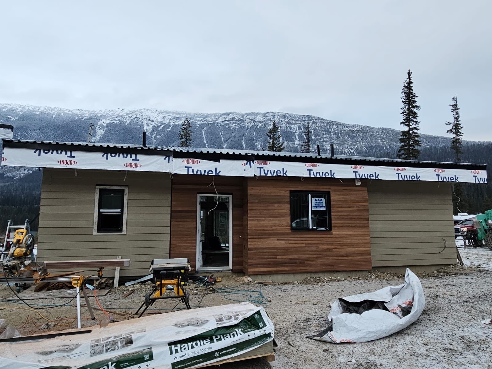 Single-storey cabin with cedar cladding going on and a snow-covered mountain behind